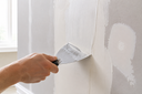 Hand applying skim coat with a putty knife to smooth and repair a wall before wallpaper installation