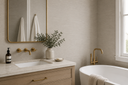 Elegant bathroom with neutral textured wallpaper, warm wood cabinetry, brass fixtures, and a freestanding bathtub.