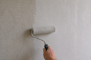 Person applying white paint over embossed damask wallpaper with a paint roller.