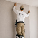 Professional installer smoothing beige textured wallpaper onto a prepared interior wall.