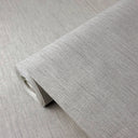 A close-up of a roll of light gray textured wallpaper with a linen-like weave pattern, partially unrolled to show the surface detail.