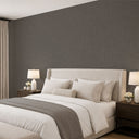 A modern bedroom featuring a large bed dressed in white linens with a taupe throw, set against a dark textured wall. The room includes dark wood nightstands with lit table lamps and neutral curtains.