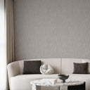 A styled living room scene featuring a textured light gray wallpaper on the wall behind a cream-colored curved sofa with dark accent pillows and a marble coffee table.