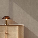 Beige textured wallpaper with a warm brown wood credenza and a bronze table lamp in a styled room setting.