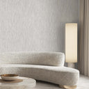 A modern curved boucle sofa in a light beige textured fabric, styled in a minimalist living room with a matching textured wallpaper, a marble coffee table, a gold bowl, and a tall floor lamp.